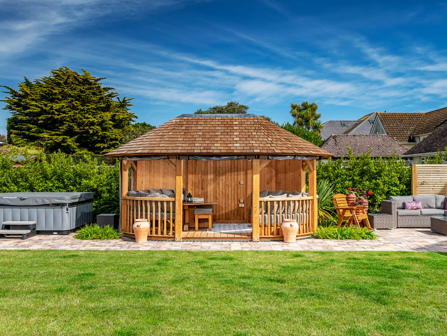 A luxury wooden gazebo in a sunny garden with hot tub
